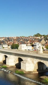 Scenic view of a historic stone bridge crossing the Loire River with traditional French village houses in La Charite sur Loire under a clear blue sky.