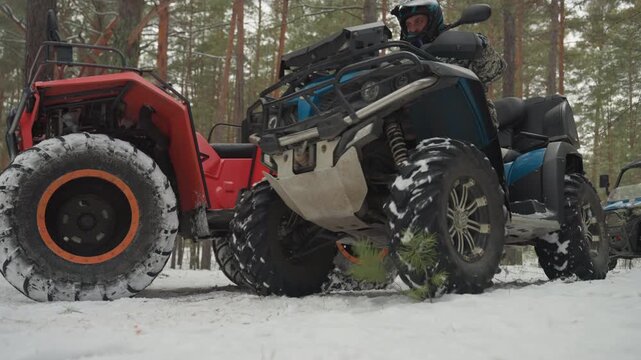 Two atvs idling with oversized tires in snowy pine clearing, closeup on tread and suspension, mechanics inspecting drivetrain and racks, riders prepare helmets, intense focus on power, grip,