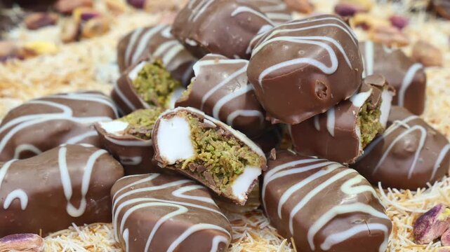 Slow motion close up of pistachio and cream filled chocolates on traditional shredded pastry background with nuts.