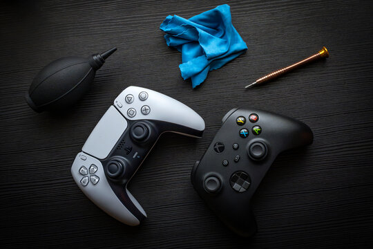 Modern PlayStation and Xbox game controllers with cleaning tools on dark wooden surface