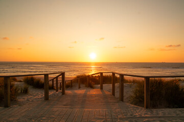 Obraz premium Wooden path at Costa Nova d'Aveiro, Portugal, over sand dunes with ocean view, evening. Wooden footbridge of Costa Nova beach . Aveiro, Portugal.
