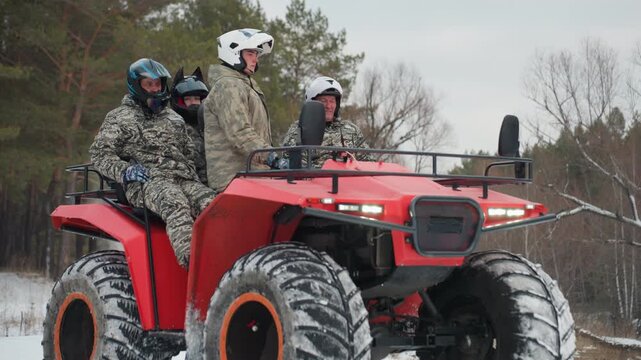 Three riders on red atv pause on snowy pine trail wearing camo jackets and helmets driver prepares to lead extreme offroad winter expedition while passengers act as navigator and spotter, engines