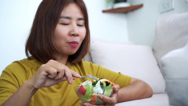 happy Asian woman enjoys eating a fresh vegetable salad . Concept of healthy dieting, clean eating lifestyle, weight loss, nutrition, and wellness at home in a living room