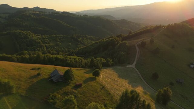 Majestic sunset backward drone flyover over traditional Carpathian hayfields with rustic wooden barns in Simon, Romania