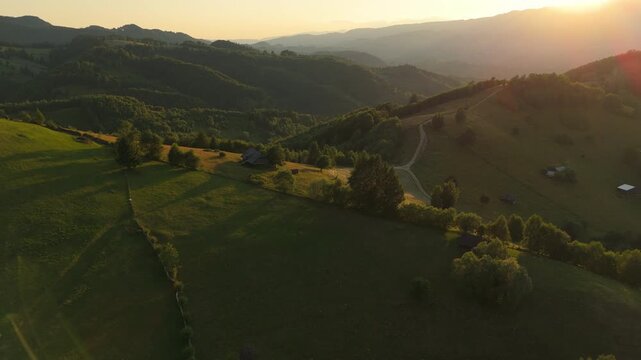 Spectacular Carpathian mountain pastures with rustic barns at golden hour sunset, a cinematic aerial drone shot flying backward in the Bran area