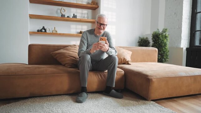 Phone addiction, aged man watching funny videos in social media, use smartphone. Portrait of laughing and smiling broadly old man resting alone in apartment, modern technology and new application