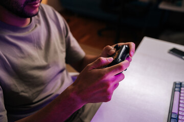Cropped shot of gamer hands holding wireless controller during video game session at home, enjoying immersive entertainment, leisure time, and technology sitting with keyboard on desk. © dikushin