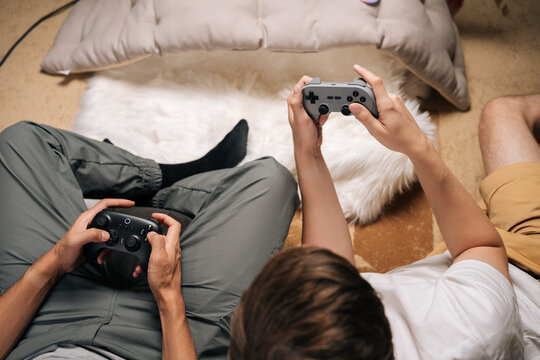 Close-up of two male friends gaming together at home, enjoying console video games during leisure time, having fun and unwinding while sharing entertaining moments and screen time.