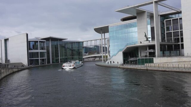 A boat moves along the river between modern government buildings in Berlin. Clean architecture and calm water reflect a contemporary urban landscape.