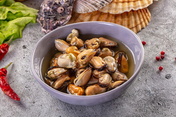 Fototapeta premium Marinated mussels in a bowl with chili peppers, lettuce, and seashells on a rustic grey background.