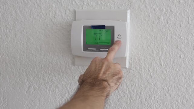 Close-up of adjusting home thermostat temperature on wall mounted HVAC system. Green display screen active. Concept of climate control, energy efficiency, and smart home technology.