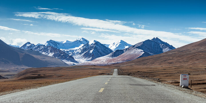 Panoramic view of 1855 milestone on Karakoram Highway (KKH), Pamir Plateau, Xinjiang, China. High-altitude border road with snow-capped mountains, vast plateau landscape, and remote mountain highway.