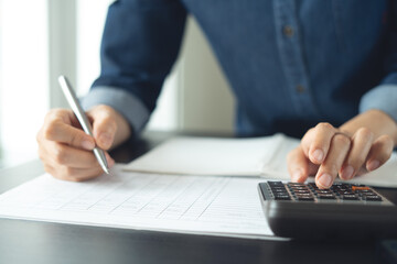 Fototapeta premium Doing finance, budgeting and tax calculation, monthly expenses. Close up, business woman using calculator to calculate financial report, accounting and budgeting, working at office
