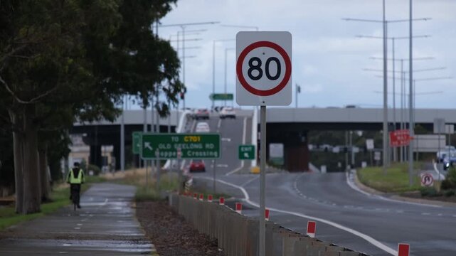 80 kmh speed limit sign on suburban arterial road with cyclist and highway overpass in Melbourne Australia. Speed control signage, traffic regulation and road safety