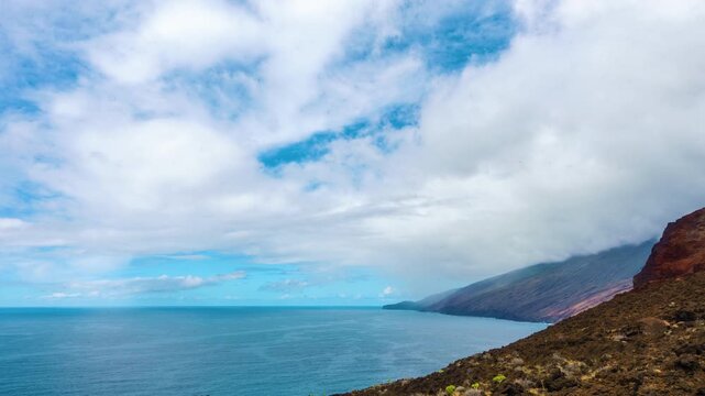 Timelapse of orographic cloud formation flowing over an island mountain ridge, with a higher cloud layer moving in a different direction, revealing wind shear and dynamic atmospheric motion