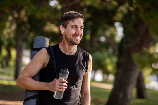 Smiling man with yoga mat and water bottle in park