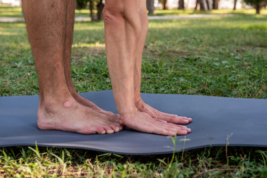 Man practicing yoga on mat outdoors, close-up of feet