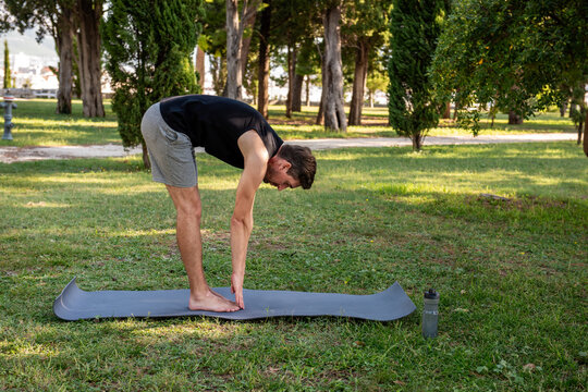 Man practicing standing forward bend yoga in city park