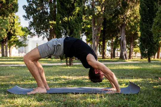 Man doing yoga wheel pose outdoors on mat in park