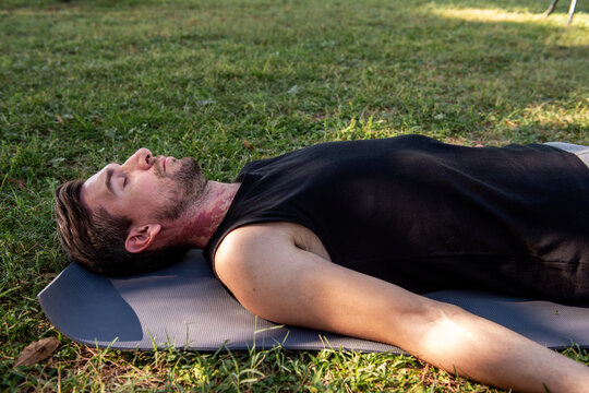Man relaxing in savasana yoga pose on park mat outdoors