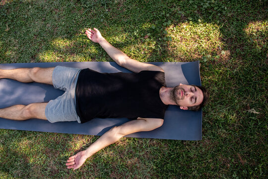 Man resting in savasana yoga pose outdoors on mat