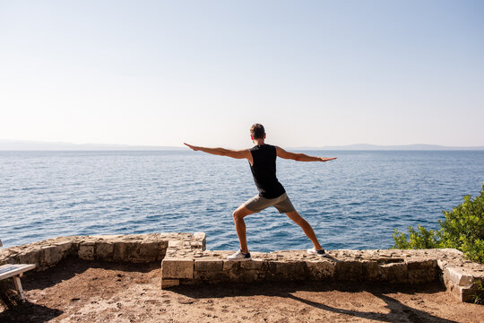 Man practicing yoga pose on seaside cliff at sunrise