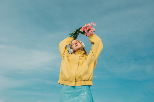 Woman in yellow jacket enjoying music with flowers
