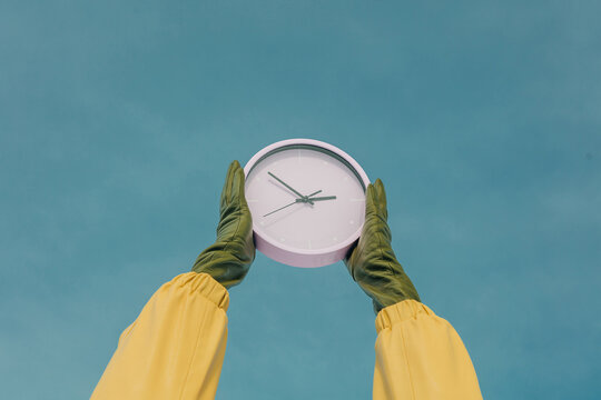 Clock held by gloved hands against blue sky backdrop