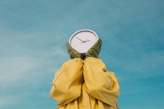 Person holding clock against blue sky in yellow coat