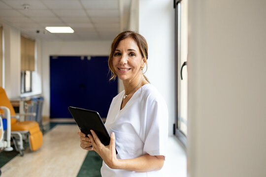Doctor with tablet smiling in hospital corridor