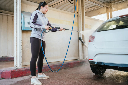 Teenager pressure washing a car at self service wash bay