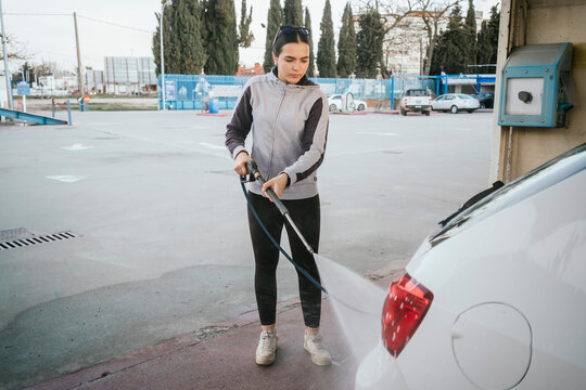 Teenager pressure washing a car at outdoor self service bay