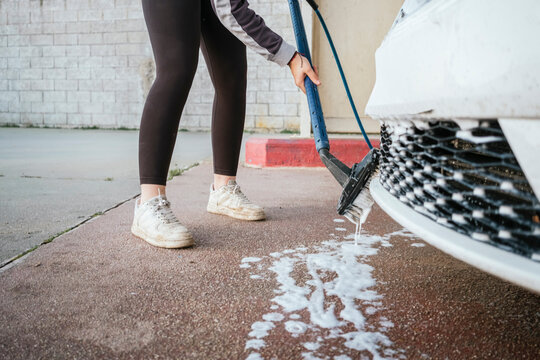 Teenager washing a car with brush and soap outdoors