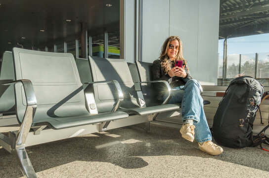 Woman waiting at station with smartphone and backpack