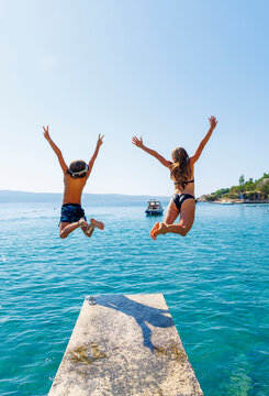 Siblings jumping into turquoise sea from a pier in Croatia. Summer vacation, happiness