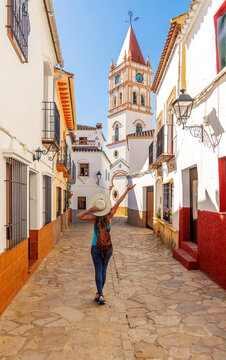 Happy woman tourist walking in La Callejuela street toward San Juan de Letran church in Arriate. Province of Malaga