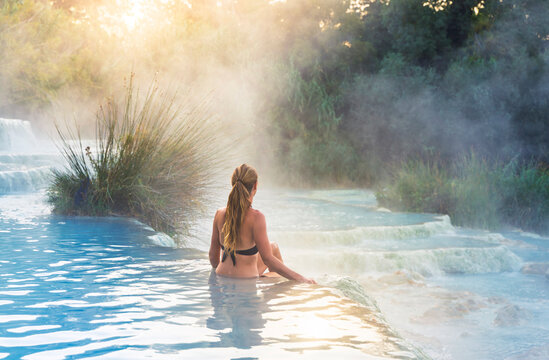 Woman sitting in Saturnia thermal springs at sunrise, concept of relaxation