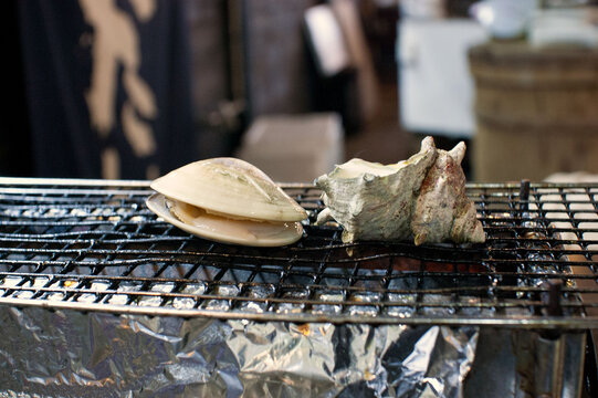 Grilled turban shell and hard clam on a wire mesh at a Japanese seafood restaurant.