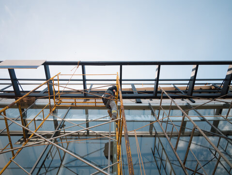 Worker on scaffold installing glass facade on modern building