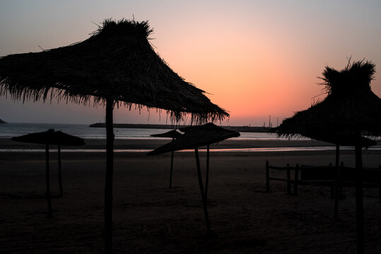 Beach sunset silhouette with straw umbrella in Marrakech