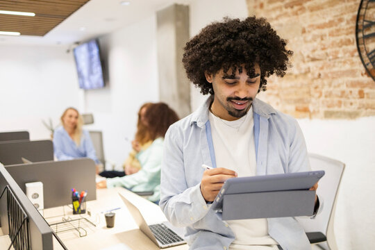 Latin man using tablet while team works in coworking