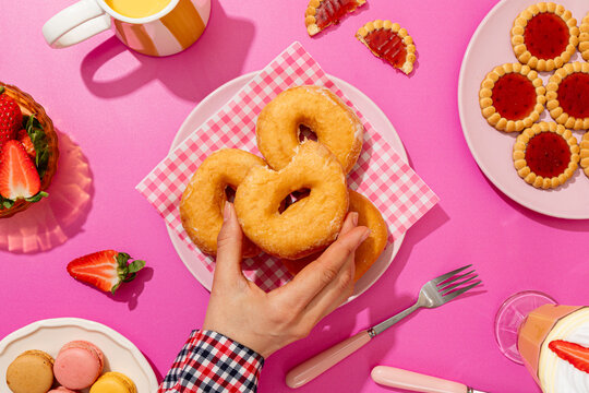Hand reaching for donuts on vibrant pink background