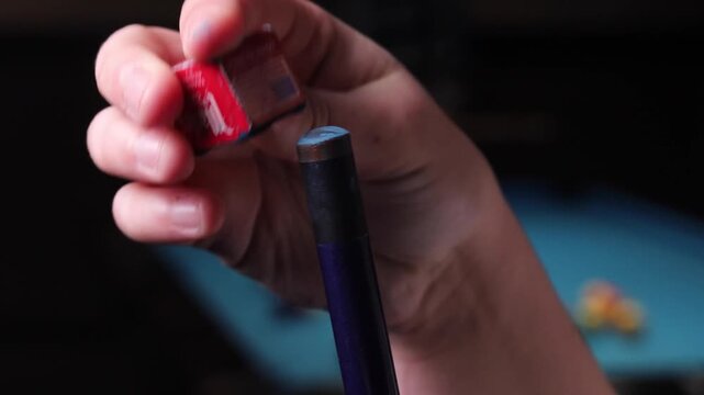 Close up view of person hands chalking a blue pool cue tip before shooting a game of billiards