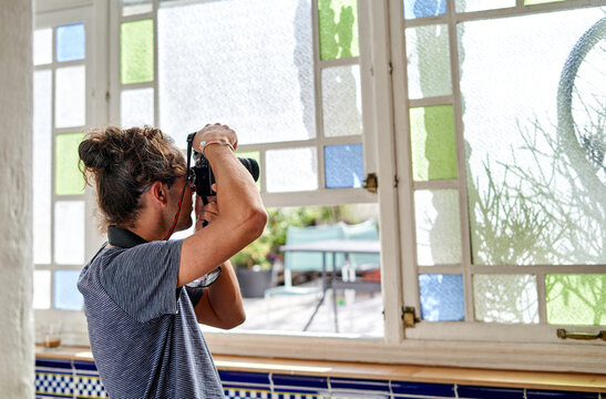 Young woman with curly hair works from home taking photos near windows