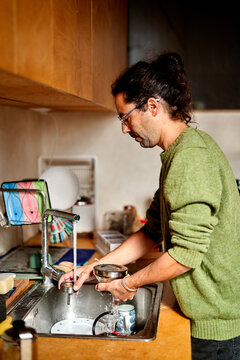 Man washing utensils while he is standing by the sink in the kitchen