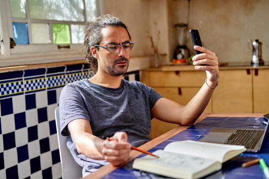 Man works from home using smartphone and notebook at kitchen table