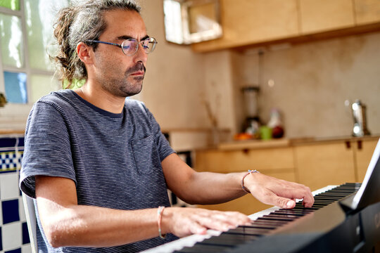 Working from home in a kitchen, a man of Hispanic descent plays piano