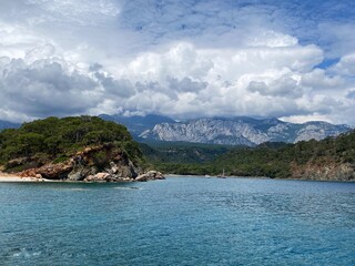 Fototapeta premium Panoramic view of the Taurus mountain range near Camyuva. Calm Mediterranean sea, blue water. Mountains in the clouds. In the distance, a closed beach surrounded by hills.