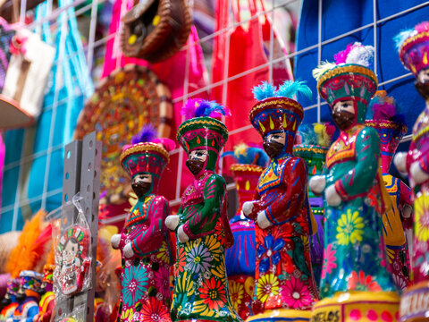 Colorful Handmade Clay Figurines in Traditional Attire Displayed on Wooden Surface. Chinelo.