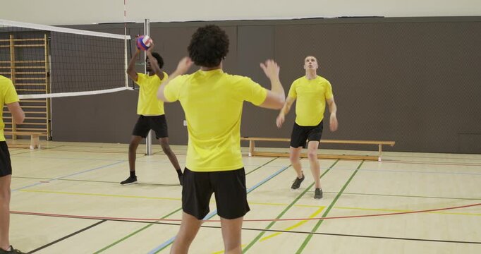 Male teammates reacting to toss, practicing passing, pushing volleyball up and blocking at gym net
